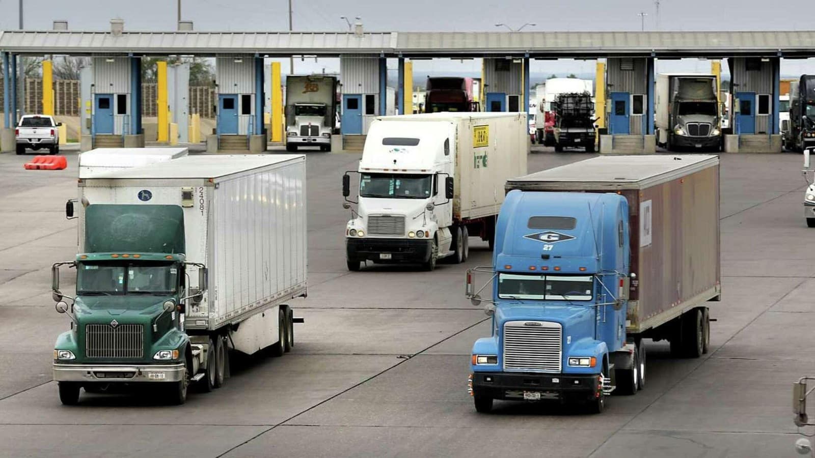 Multiple freight trucks moving through inspection or customs booths